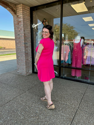 Woman wearing bright pink flutter dress standing outside clothing boutique storefront