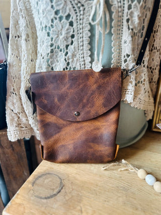 Brown leather crossbody bag with envelope flap and adjustable strap displayed on wooden surface