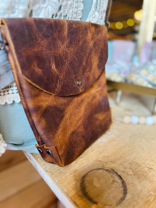 Brown leather crossbody bag with flap closure and adjustable strap displayed on wooden surface