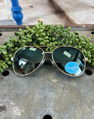 Aviator-style sunglasses with gold frames and dark lenses on wooden surface with green succulent plant