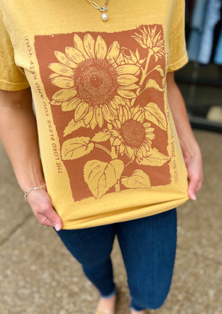 Woman wearing yellow t-shirt with sunflower design and "The Lord Bless You" text print