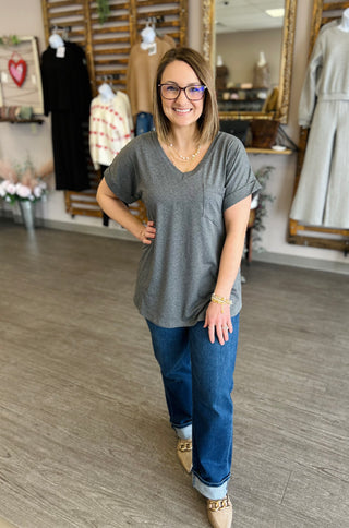 Woman wearing gray pocket tee and jeans standing in clothing boutique with mirror and displayed apparel.