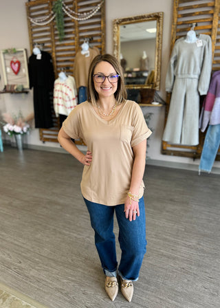 Woman wearing beige relaxed-fit pocket tee with jeans and accessories in clothing boutique setting.