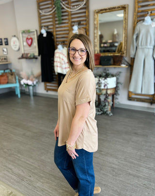 Woman wearing beige pocket tee and jeans standing in boutique store with clothing displays and mirror.