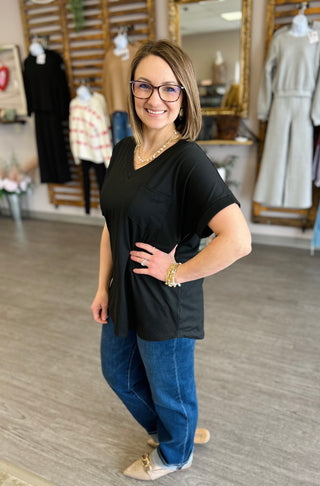 Woman wearing black pocket tee and jeans in retail clothing store with displayed garments