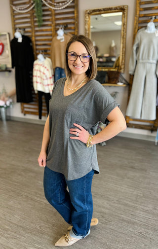 Woman wearing gray pocket tee and jeans posing in clothing boutique with vintage mirror and displays.