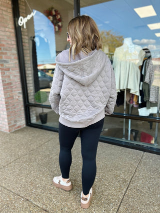 Woman wearing quilted hooded sweatshirt and leggings walking past storefront window display