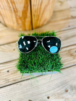 Aviator sunglasses with dark lenses resting on artificial grass against wooden deck background