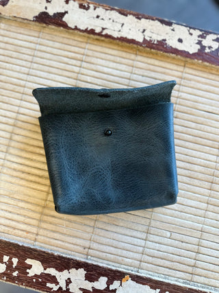 Black leather Wendy Wallet with snap closure displayed on bamboo mat surface