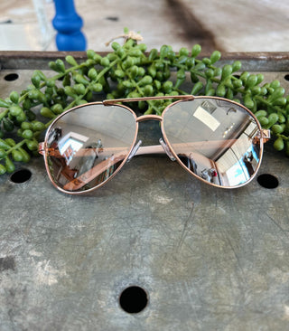 Rose gold aviator sunglasses with mirrored lenses displayed on wooden surface with green succulent plant