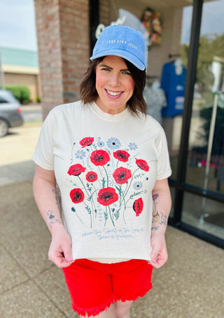 Woman wearing floral patriotic t-shirt with red poppies and blue flowers, paired with red shorts and blue cap.
