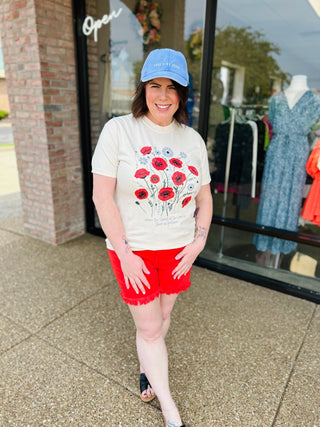 Woman wearing patriotic floral t-shirt with red shorts and blue cap standing outside storefront
