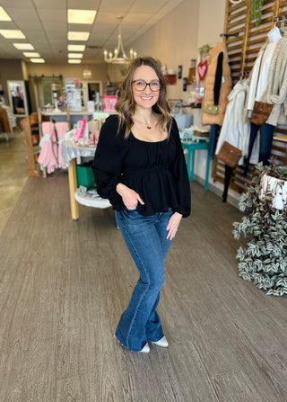 Woman wearing black long-sleeve blouse with jeans standing in boutique store setting
