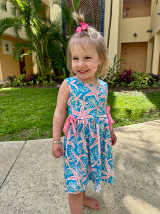 Young girl wearing tropical print sleeveless dress with pink bow accents in outdoor setting