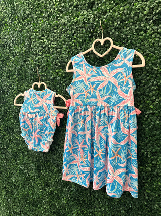 Tropical palm print dress for girls displayed on heart-shaped hanger with matching doll outfit on green backdrop.