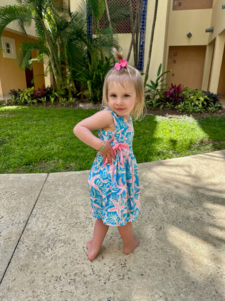 Young girl wearing tropical print sleeveless dress with pink and blue floral pattern, standing outdoors