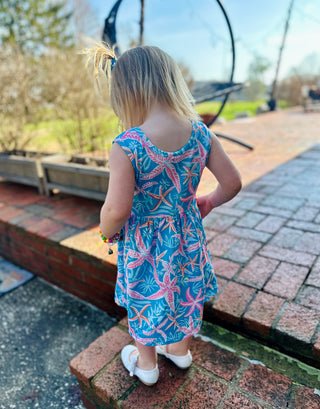 Young girl wearing colorful tropical print dress standing on brick pathway in outdoor setting