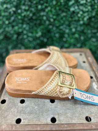 TOMS women's woven sandals with buckle detail on wooden surface with greenery background