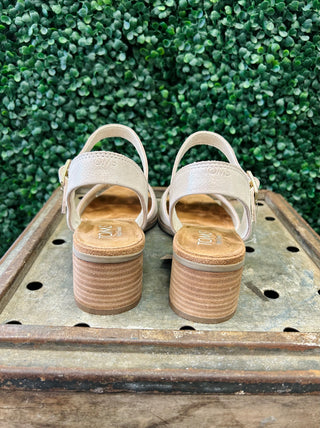 TOMS Eloise sandals with block heels and ankle straps displayed on wooden surface against green foliage background.
