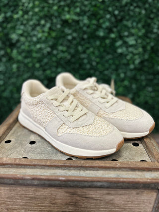 Cream colored sneakers with crochet detailing and lace-up closure on wooden surface