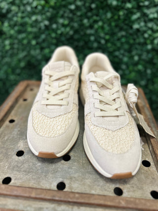 TOMS sneakers with crochet detailing and laces displayed on wooden surface with green foliage background