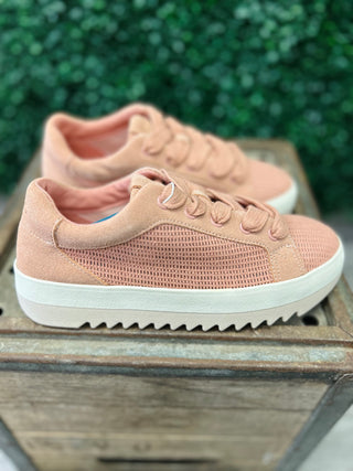 Pink mesh sneakers with lace-up closure and white sole displayed on wooden surface outdoors.