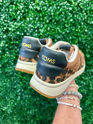TOMS leopard print sneakers with navy heel tab held against green sparkly background