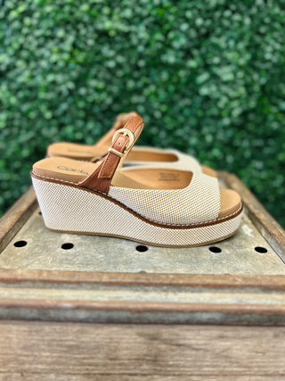 Corkys Treat Yourself platform wedge sandals with textured upper and brown ankle strap on wooden surface.