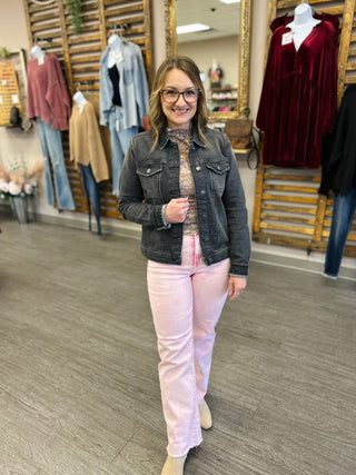 Woman modeling pink straight jeans with denim jacket in clothing store with mannequins displaying various outfits