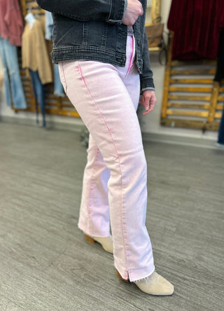 Woman wearing pink straight-leg jeans with dark denim jacket and tan boots in retail setting.