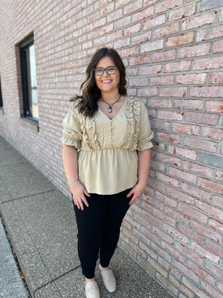 Woman wearing polka dot ruffle detail puff sleeve top with black pants against brick wall
