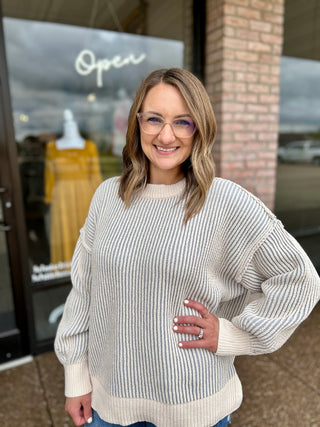 Woman smiling outside boutique wearing a ribbed two-tone crew neck pullover sweater with balloon sleeves.