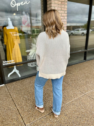 Woman wearing a ribbed two-tone oversized sweater with jeans and sandals, back view.