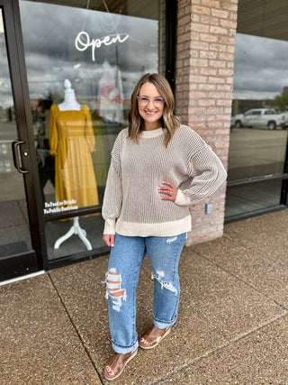 Woman wearing a ribbed two-tone crew neck sweater with balloon sleeves outside a boutique storefront.