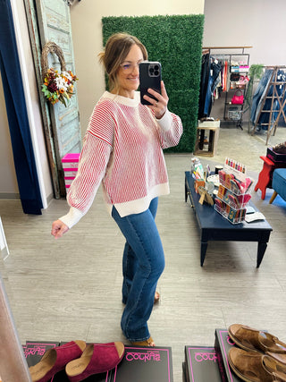 Woman wearing a striped red and white ribbed knit sweater with blue jeans in a boutique.