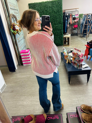 Woman wearing a striped ribbed knit sweater with flare jeans, shown from behind in boutique mirror selfie.