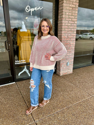 Woman wearing a striped two-tone knit sweater paired with distressed jeans and wedge sandals.