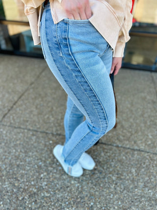 Woman wearing light wash skinny jeans with frayed hem and white sneakers on concrete surface.