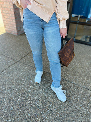 Person wearing two-tone skinny jeans with frayed hem, beige top, white sneakers, carrying brown bag.