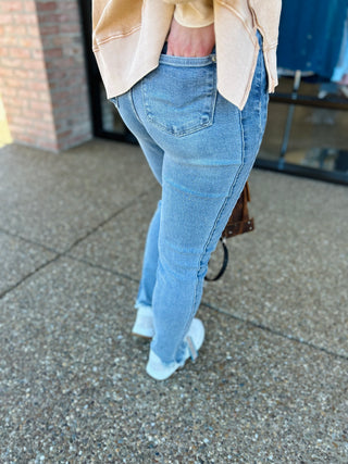 Woman wearing light wash skinny jeans with frayed hem and beige blazer walking outdoors