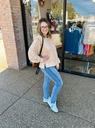 Woman wearing beige sweatshirt and two-tone fray hem skinny jeans standing outside boutique storefront
