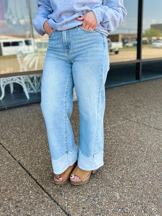 Woman wearing wide leg jeans with two-tone hem detail, paired with platform sandals and gray sweatshirt.