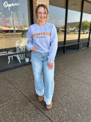 Woman wearing wide leg jeans with two-tone hem detail, paired with a seasonal sweatshirt and heeled sandals.