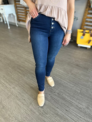 Woman wearing dark wash skinny jeans with button fly detail, styled with beige top and loafers.