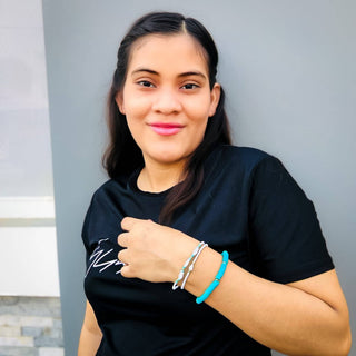 Woman wearing turquoise and silver beaded bracelets, smiling while posing with arms crossed in casual black top.