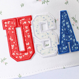 White trucker hat featuring red, white, and blue floral embroidered USA patch lettering.
