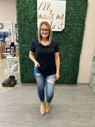 Woman wearing black v-neck basic tee with distressed jeans and tan boots in boutique setting