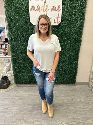 Woman wearing white v-neck basic tee with distressed jeans and tan boots in boutique setting.