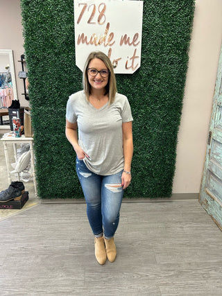 Woman wearing gray v-neck basic tee with distressed jeans and ankle boots in boutique setting.