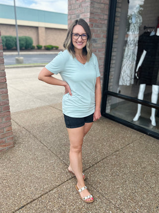 Woman wearing light blue v-neck basic tee with denim shorts, standing outdoors smiling.